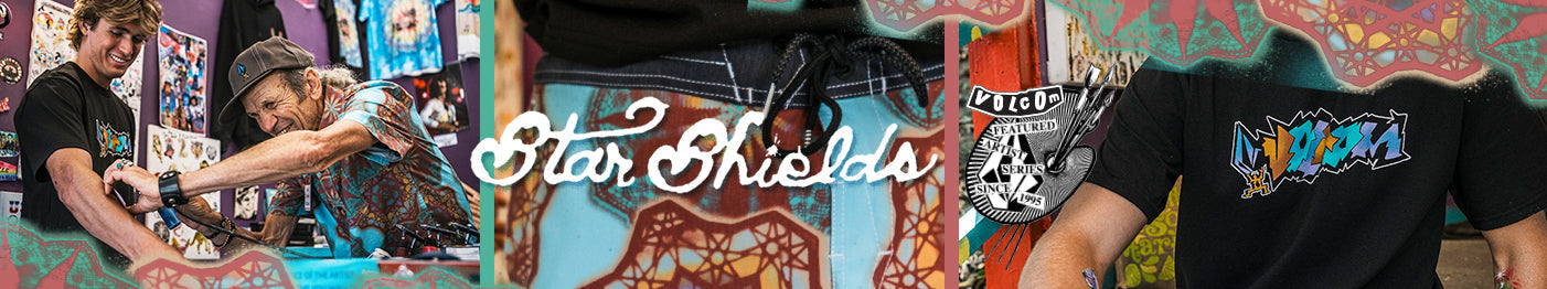 Two people smiling and working together in a colorful shop with bold, artistic shirts and a close-up of a black t-shirt with a vibrant design. “Star Shields” is written in the center.