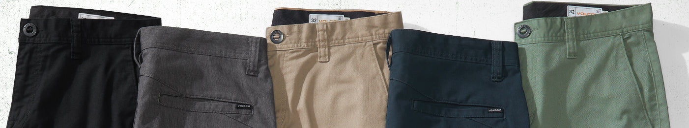 Five pairs of pants in black, gray, khaki, navy blue, and green are neatly arranged in a row, viewed from the waistbands and fronts, with visible buttons and pockets.