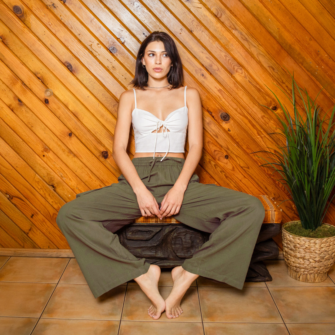 Woman sitting on a wooden bench against a wooden paneled wall with a plant to her right.