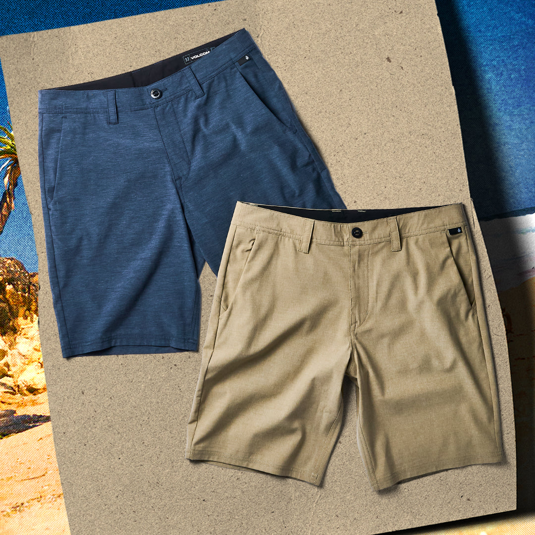 Two pairs of shorts, one blue and one beige, on a textured surface with a beach scene in the background.