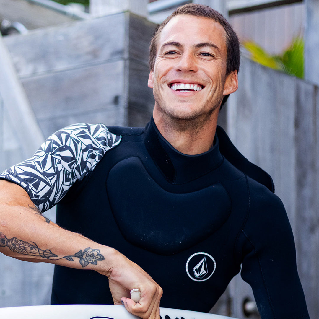 Man in a wetsuit holding a surfboard with a blurred background