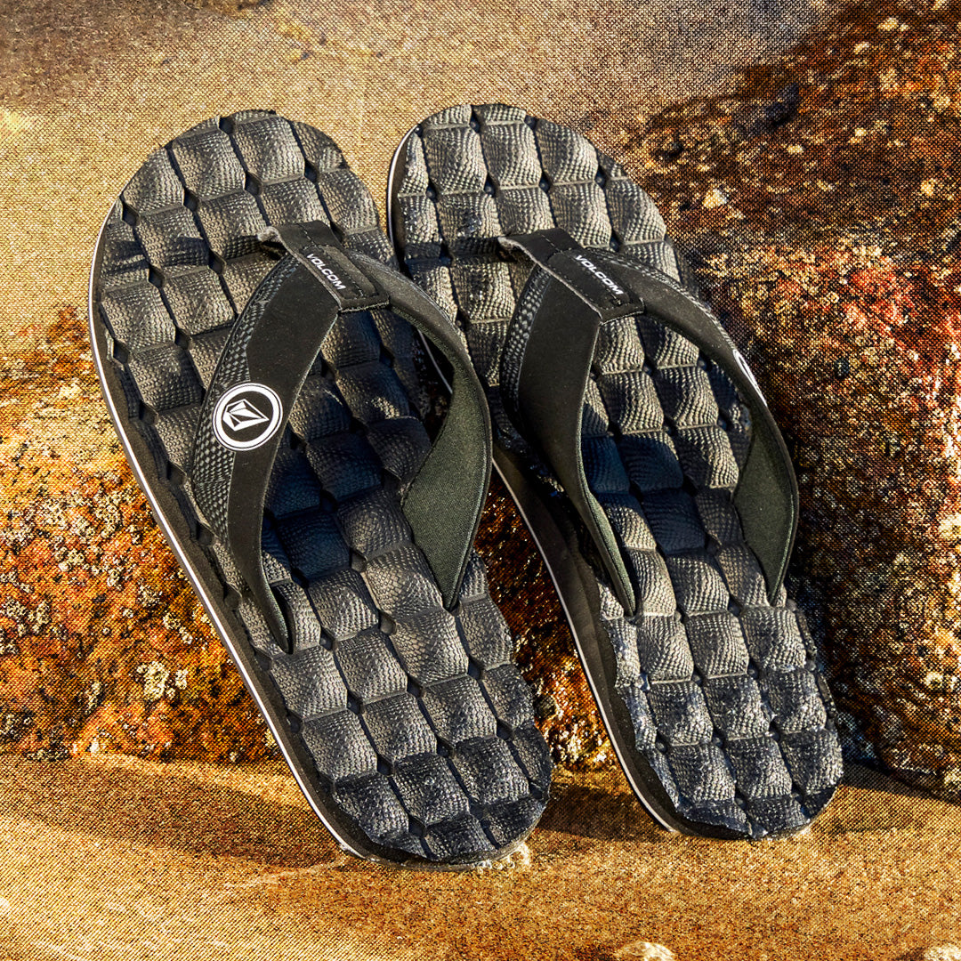 Pair of black sandals with textured sole on a textured surface
