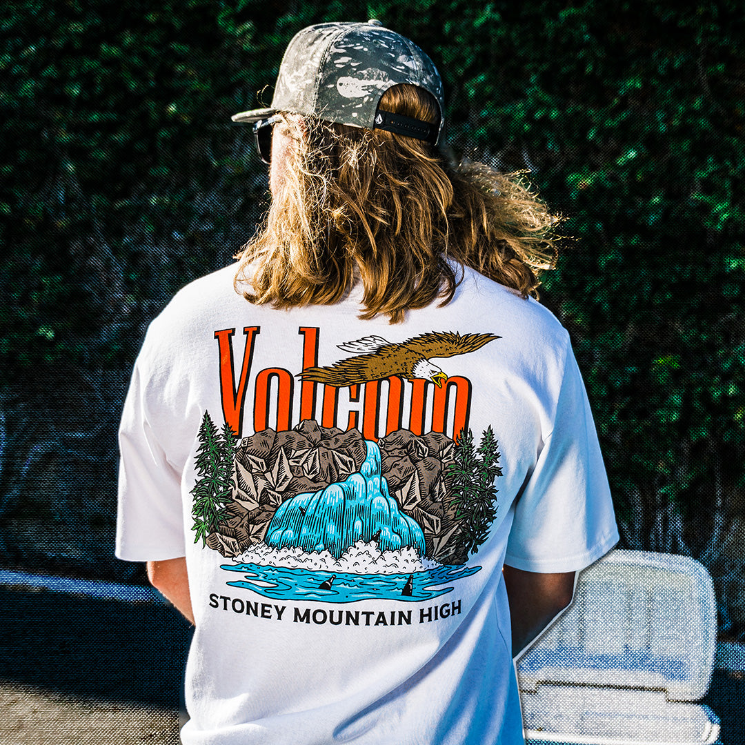 Person wearing a white t-shirt with a mountain graphic and text, standing outdoors.
