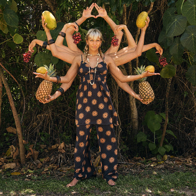 Person with multiple arms holding fruits and plants in a forest setting