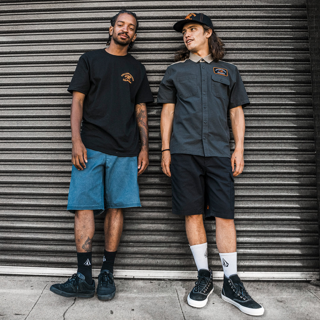 People wearing logo-branded dark shirts and shorts leaning against a garage door