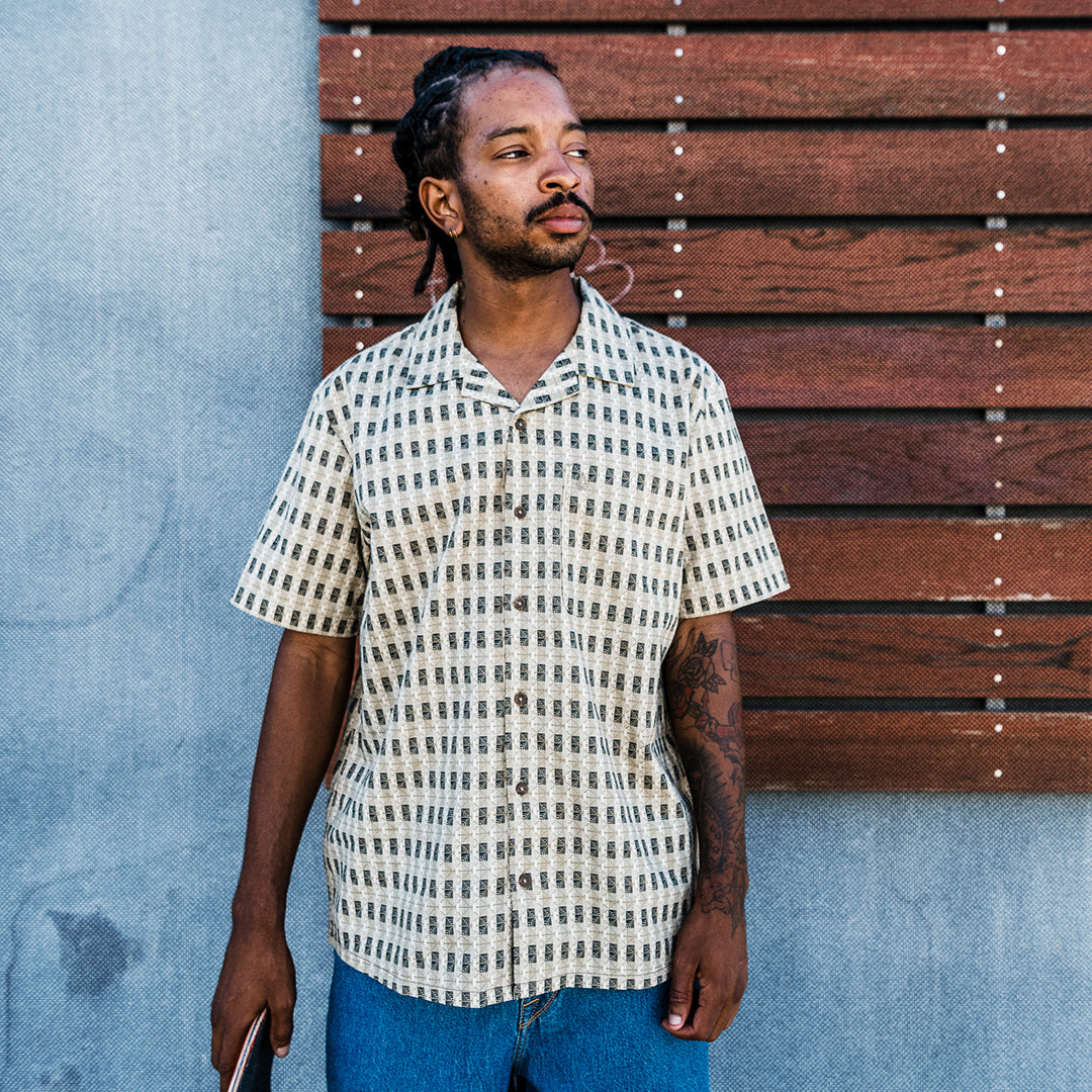 Man in white plaid button-up standing outside against wood panels