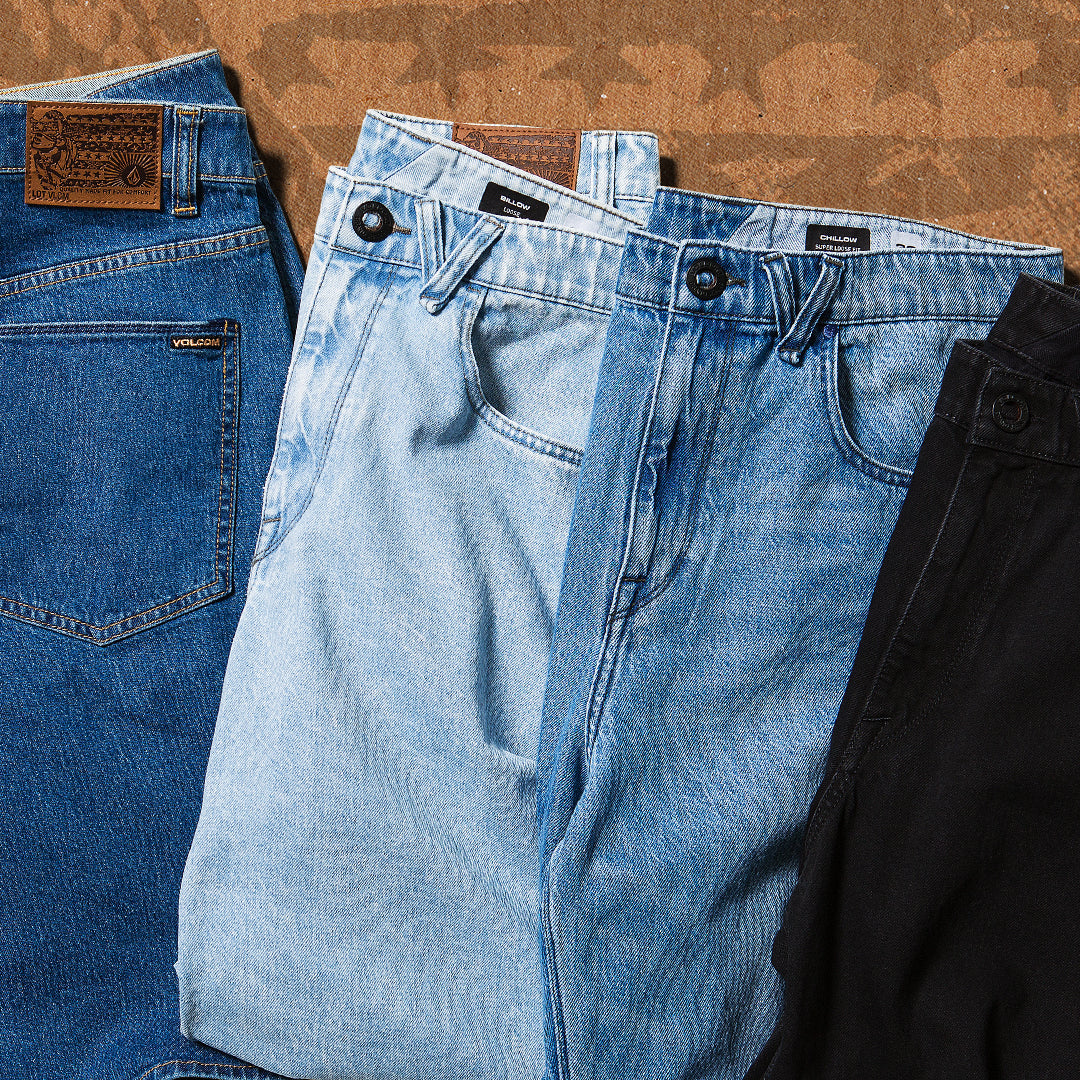 Four pairs of jeans in different colors arranged on a textured surface.