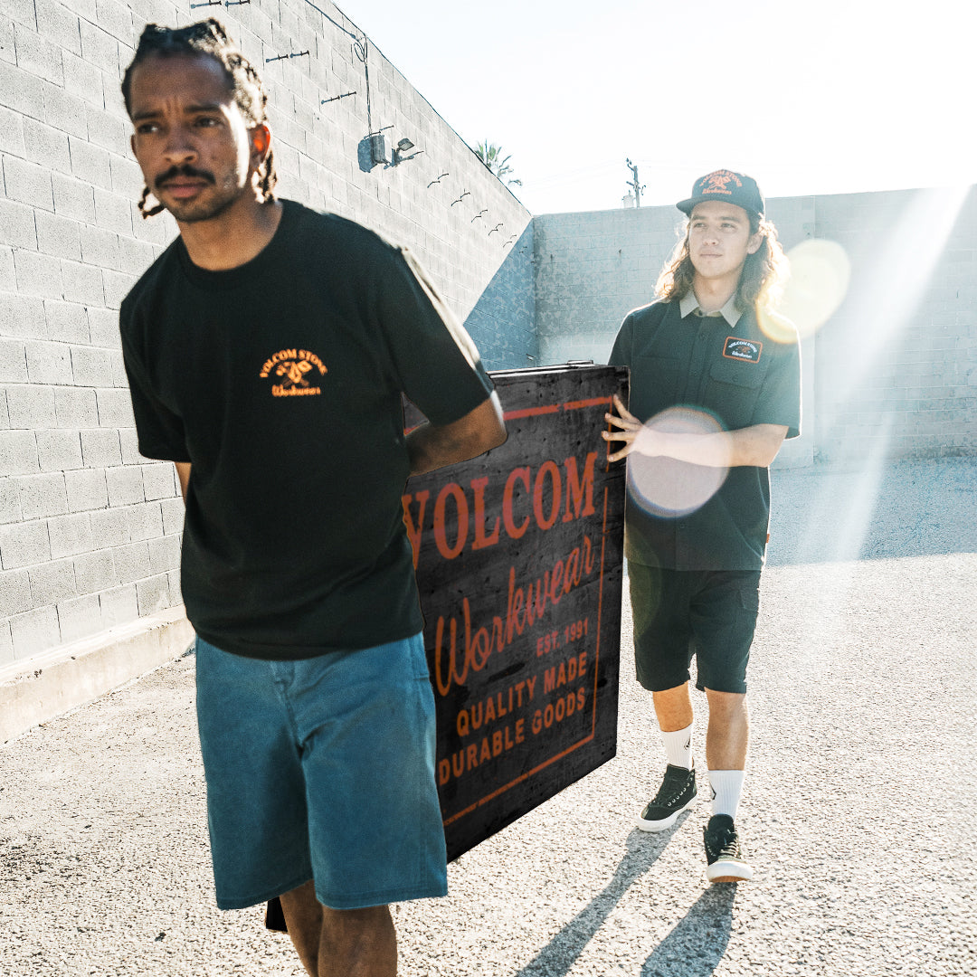 Two people holding a Volcom Workwear sign outdoors.