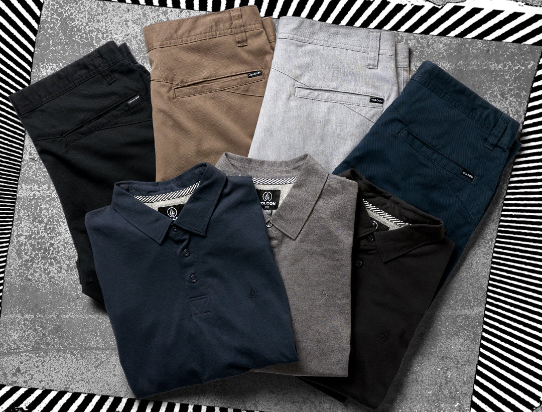 Six folded garments arranged in a fan-like flat lay: four collared polo shirts in black, gray, navy, and heather gray, with two pairs of pants in black and tan. The garments are photographed on a textured gray surface with a black-and-white striped border around the edges.