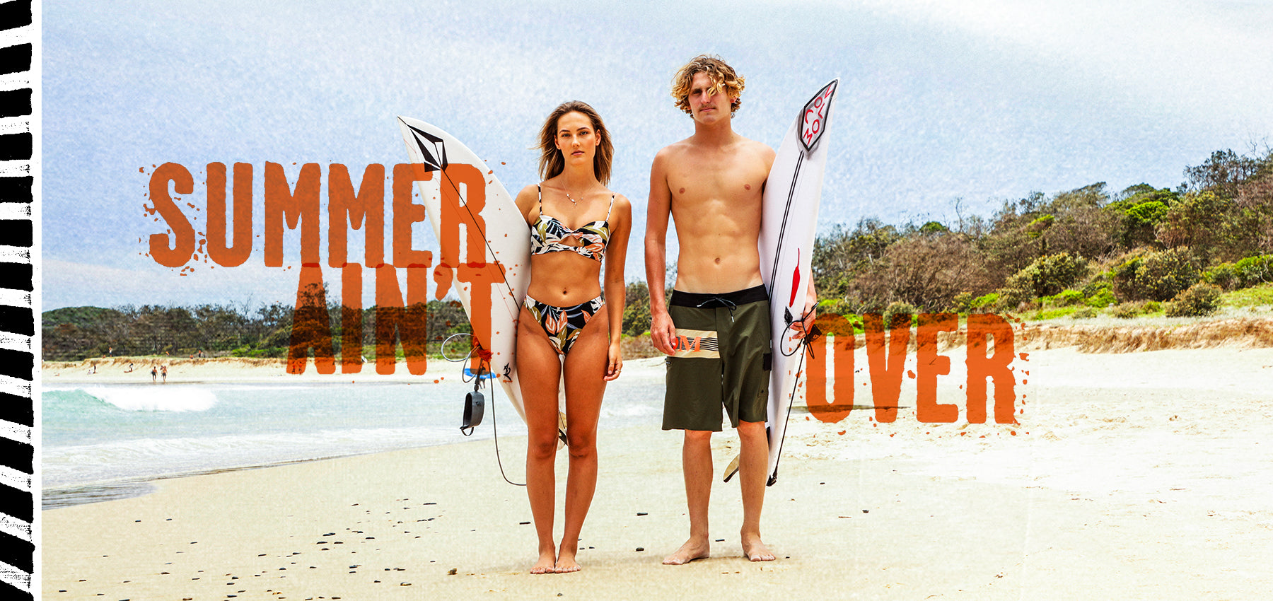 A man and a woman standing on a sandy beach holding surfboards, with large orange text reading 'SUMMER AIN'T OVER' across the scene.