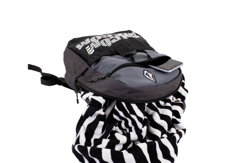 A Volcom Men's Summer School lightweight black and gray backpack, shown on a plain white background, features a convenient laptop sleeve, with a phone in the front pocket and a black-and-white striped towel partially tucked inside.