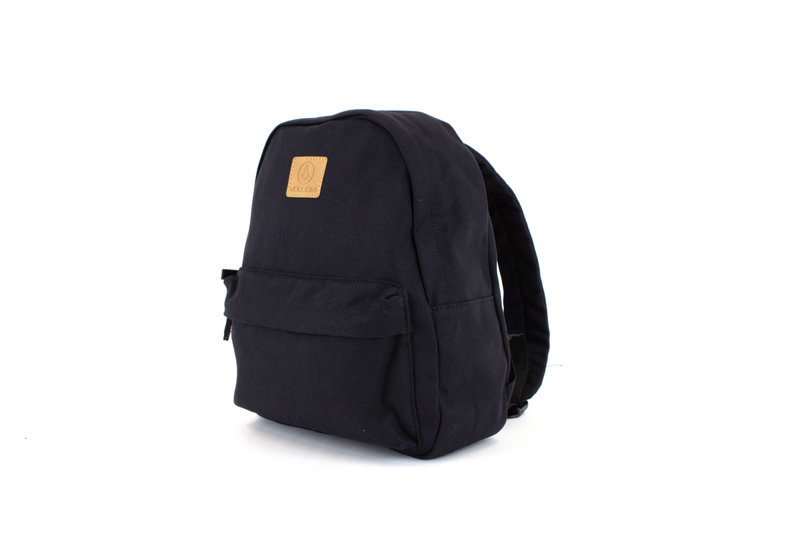 A side-angle view of the Volcom Women's Winnie Backpack in solid black, ideal for carrying your everyday essentials, featuring a tan square patch with the Volcom logo on the front, set against a plain white background.