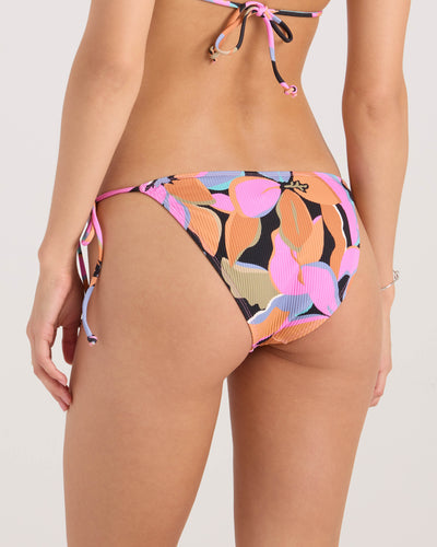 A woman is modeling the Volcom Women's Not So Sweet Full Tie Side bikini bottom, featuring a colorful leaf pattern in pink, orange, black, blue, and beige. The image shows her waist down from the back.