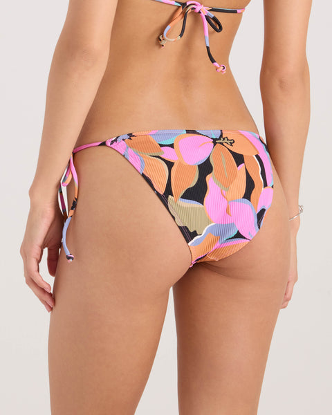 A woman is modeling the Volcom Women's Not So Sweet Full Tie Side bikini bottom, featuring a colorful leaf pattern in pink, orange, black, blue, and beige. The image shows her waist down from the back.