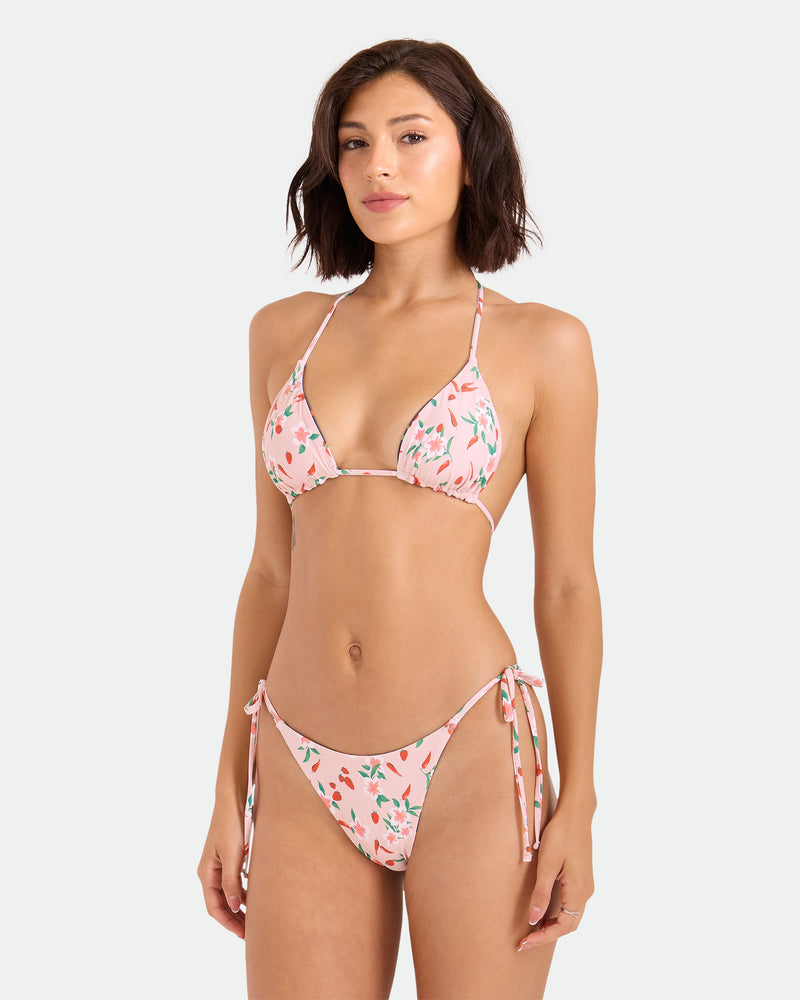 A woman with short brown hair models the Volcom Women's Sweet & Spicy Reversible Triangle Top, a light pink cherry print bikini with adjustable tie straps and side ties, against a plain white background.