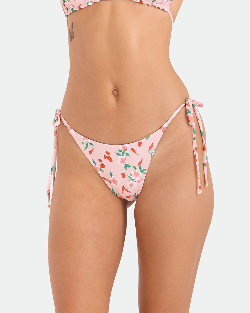 A woman models the Volcom Women's Sweet & Spicy Tie Side Teeny Reversible Bikini Bottom, featuring adjustable tie sides, with her midsection and upper thighs visible against a plain white background.