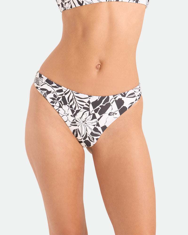 A person models the Volcom Women's Hibiscus Diamond Midrise Skimpy Reversible Bikini Bottom, featuring a black and white floral pattern, shown from mid-torso to upper thighs against a plain background.