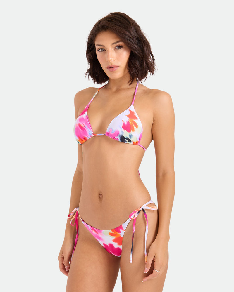 A woman with short brown hair wears the Volcom Women’s In A Daze Triangle Top bikini, crafted from recycled nylon and featuring adjustable tie straps, standing against a plain white background and looking at the camera.