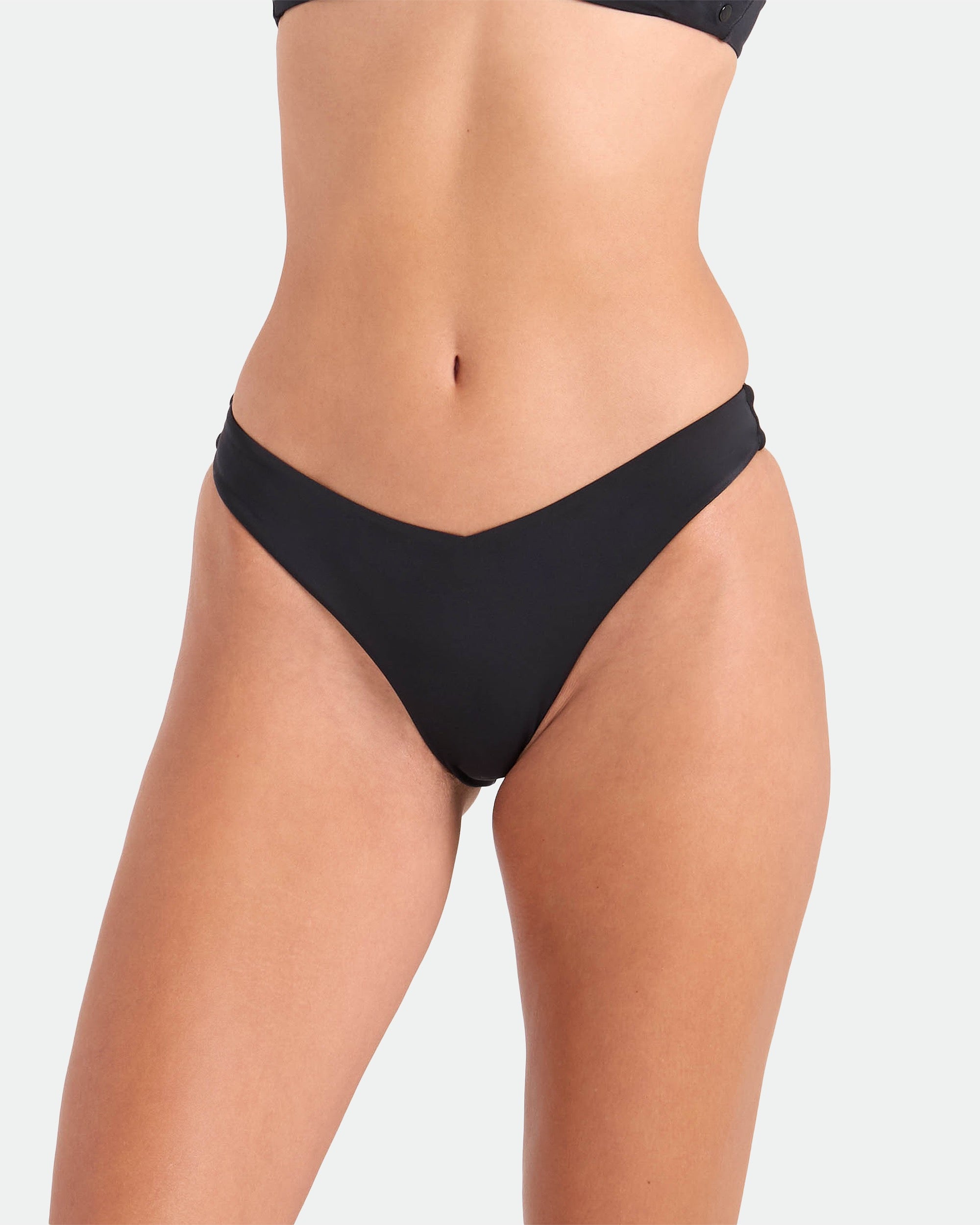 A person wears the Volcom Women's Coco Legacy Drop 90S V Bottom bikini, crafted from recycled nylon, paired with a matching top. The photo shows the torso and upper legs against a plain light background.