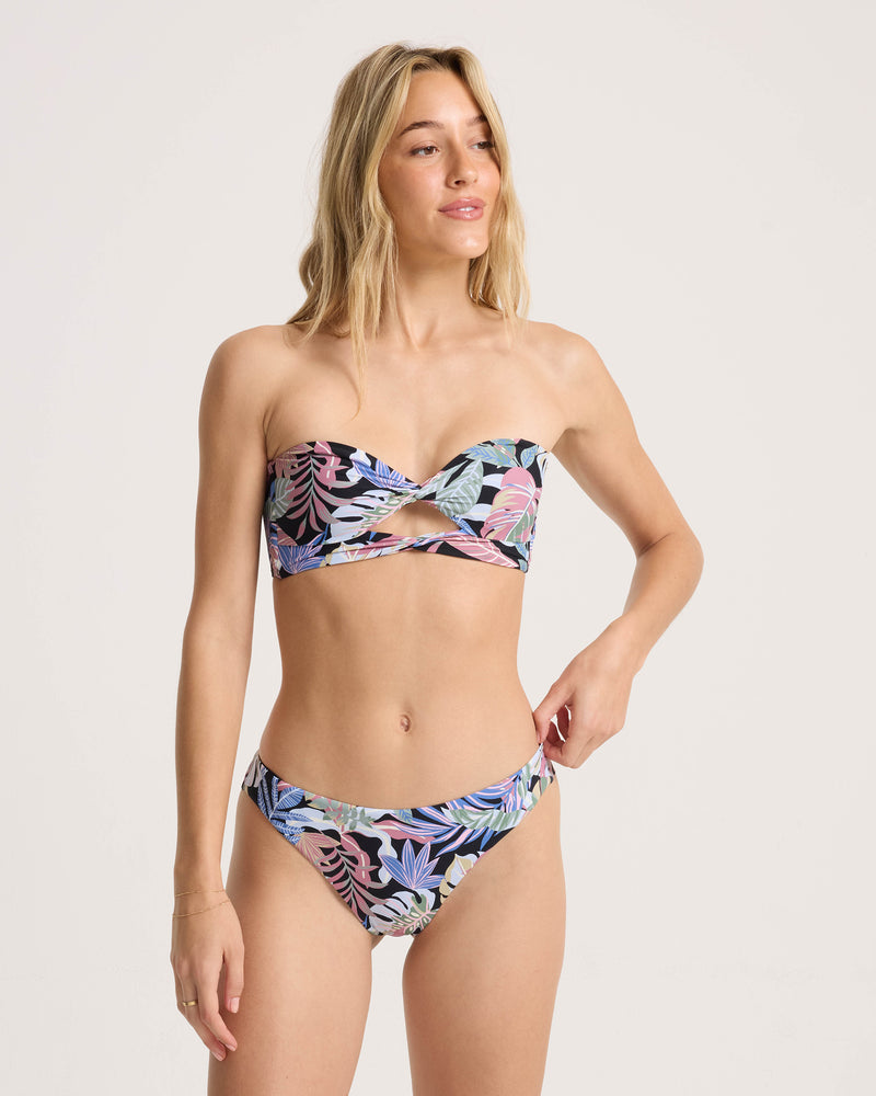 A woman models the Volcom Women’s Trop Till You Drop Hipster Cheekini in a colorful print against a plain white background.