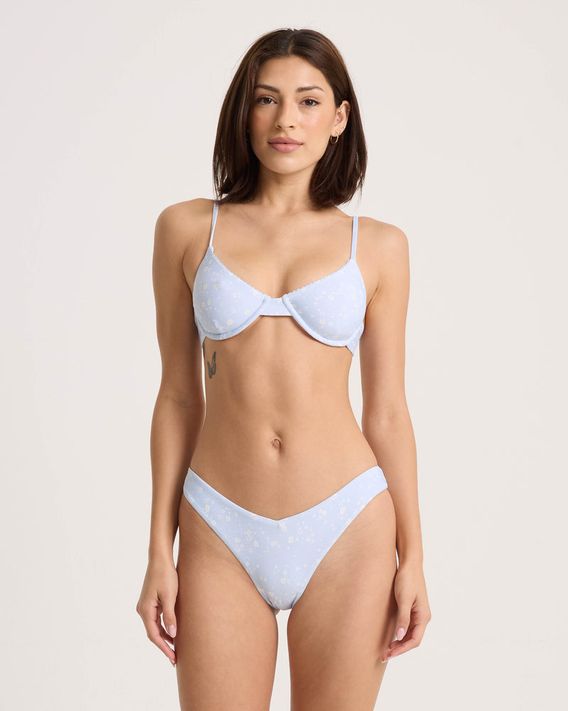 A model wears a light blue floral-patterned Volcom Women’s Ditsy Era Demi Underwire swimsuit featuring a demi cut, underwire bra top.