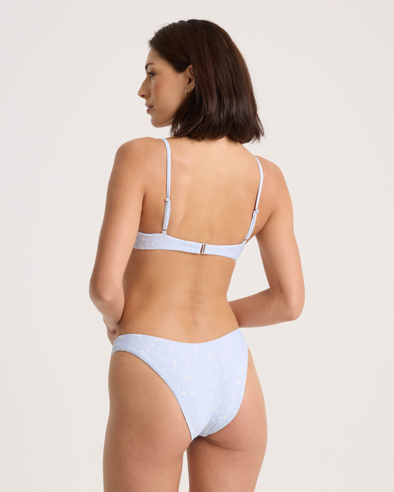 A woman seen from behind wearing a light blue Volcom Women’s Ditsy Era Demi Underwire bikini with a white floral pattern.
