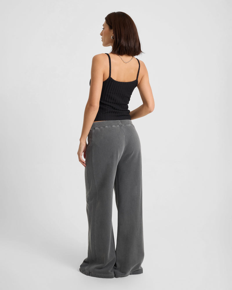 A woman faces away, wearing the Volcom Women's Lived In Rib Tank in black with loose-fitting, wide-leg gray pants, set against a plain white background.