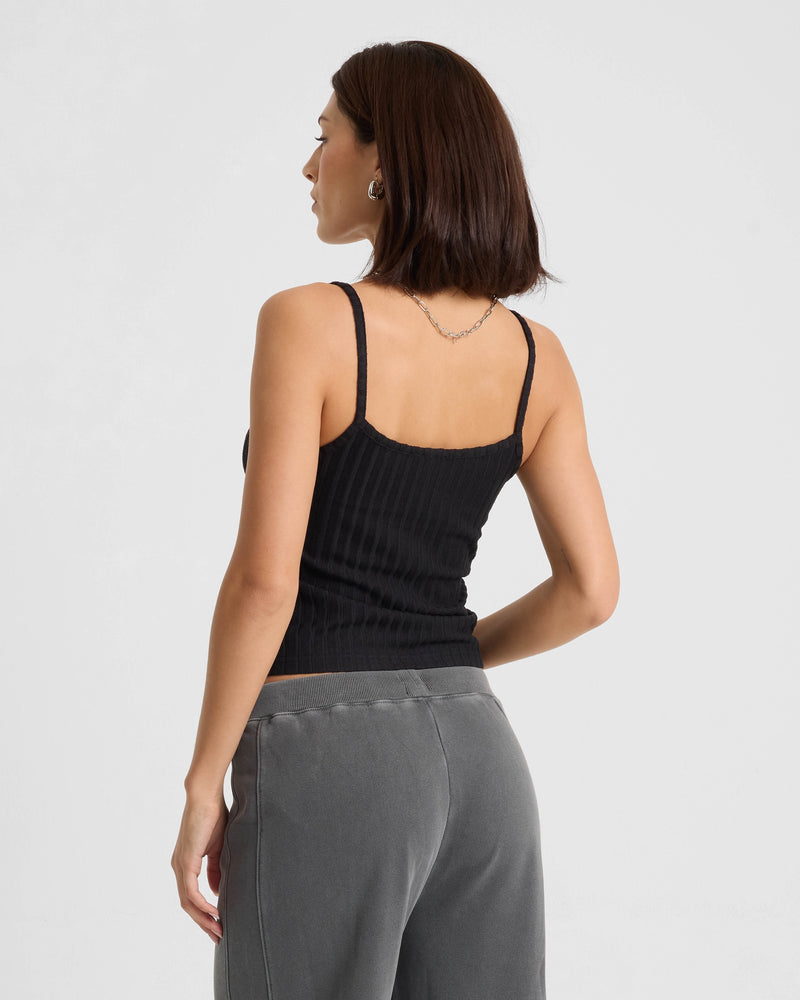 A woman with shoulder-length dark hair wears a Volcom Women's Lived In Rib Tank in black and gray pants, standing with her back to the camera against a plain light background.
