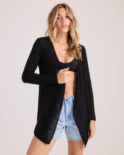 A woman poses confidently in the Volcom Women's Lived In Go Go Wrap, layered over a black bikini top and light blue denim shorts, set against a plain light background.