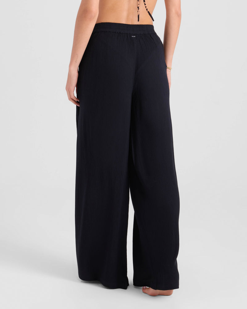 A barefoot model, shown from the waist down, wears Volcom’s Women's Stoneshine Junki Pants. The elastic waist and wide leg create a relaxed fit, while the viscose fabric drapes fluidly against a light background for a stylish look.