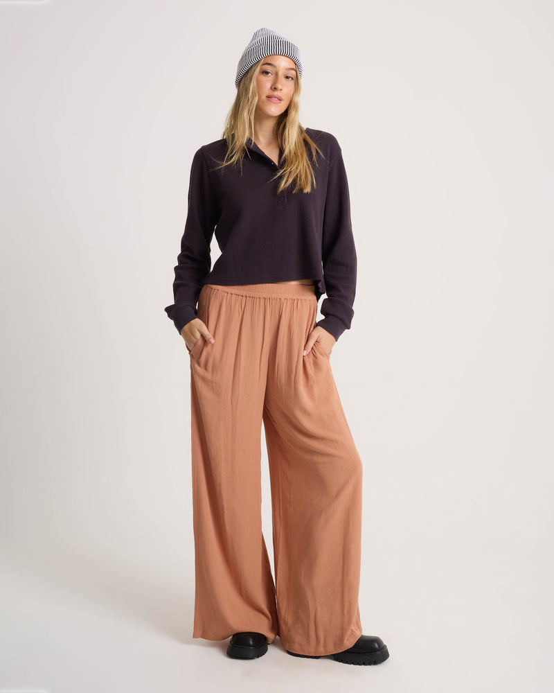 A woman wears a black long-sleeve polo shirt and a striped beanie with Volcom Women’s Stoneshine Junki Pant in peach.