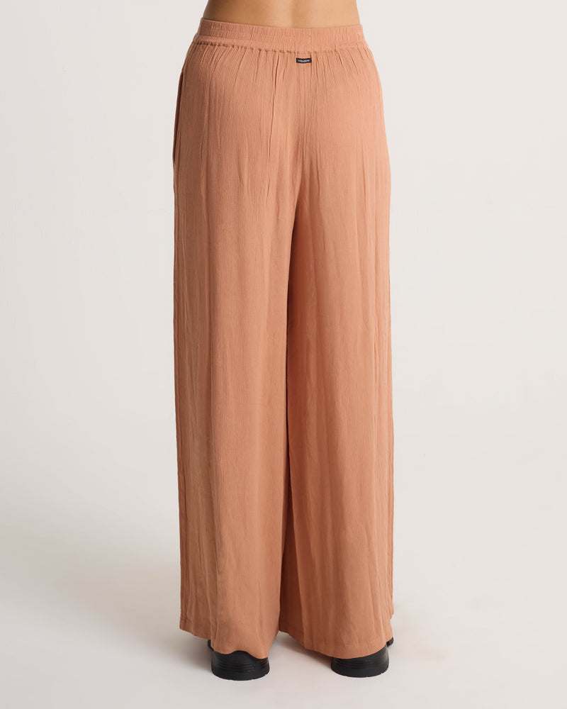 Back view of light brown, relaxed fit wide-leg Volcom Women’s Stoneshine Junki Pant with an elastic waistband.