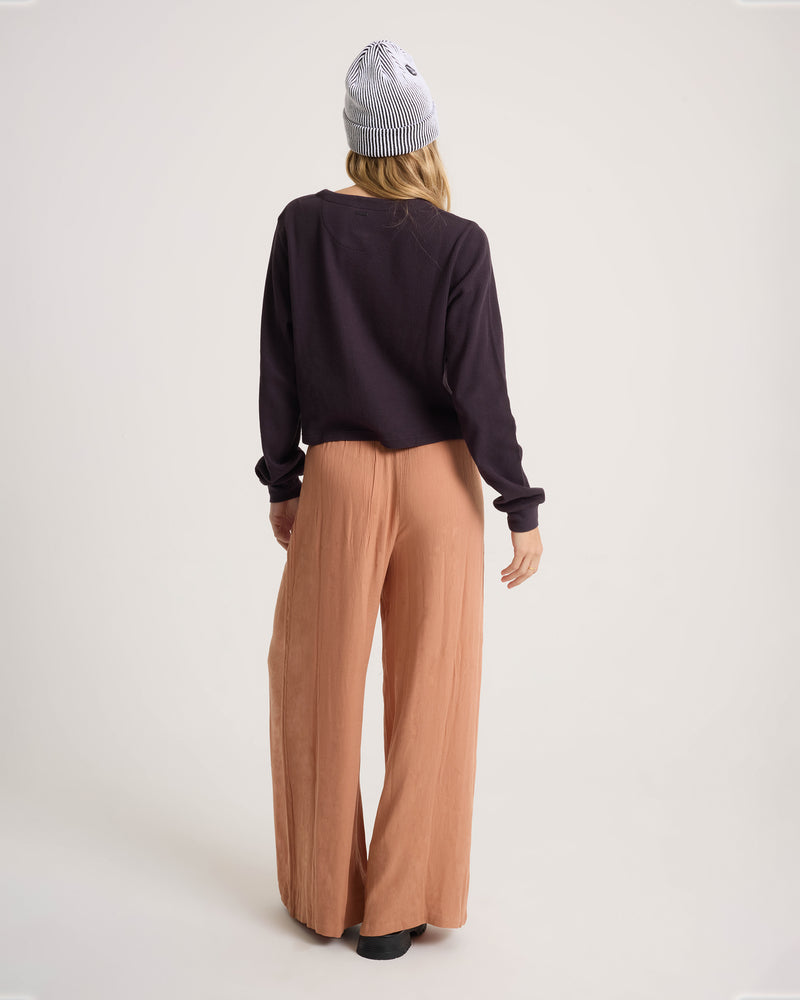 A person seen from behind, wearing a black long-sleeved shirt, relaxed-fit tan Volcom Women’s Stoneshine Junki Pant, and a striped beanie.