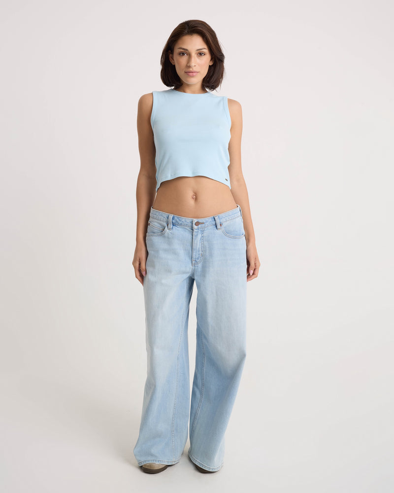 A woman faces forward against a plain light background, wearing the Volcom Women's Mary Mack Tank in light blue and loose-fitting light blue jeans.