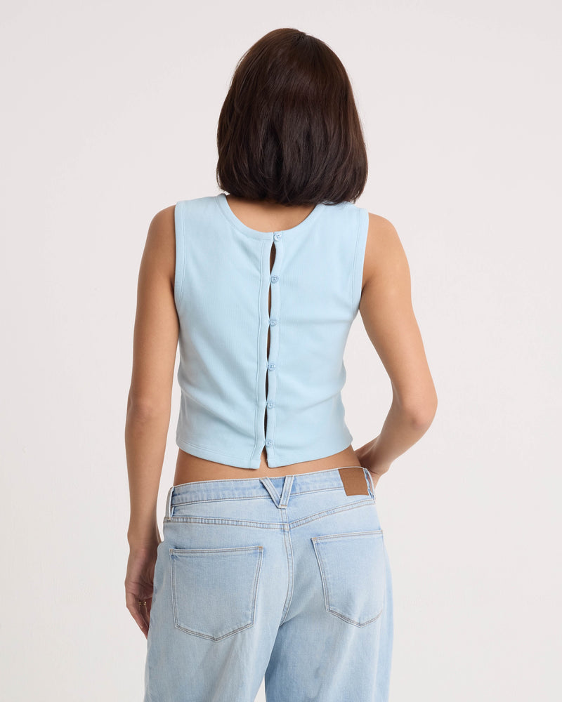 A woman, seen from behind against a white background, wears the Volcom Women's Mary Mack Tank in light blue with button details and a stretchy knit crew neck, paired with matching light blue jeans.