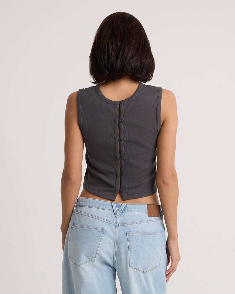 A person with short dark hair, seen from behind, wears the Volcom Women's Mary Mack Tank in Vintage Black—a cotton blend sleeveless crew-neck top featuring buttons down the back—paired with light blue jeans against a plain light background.
