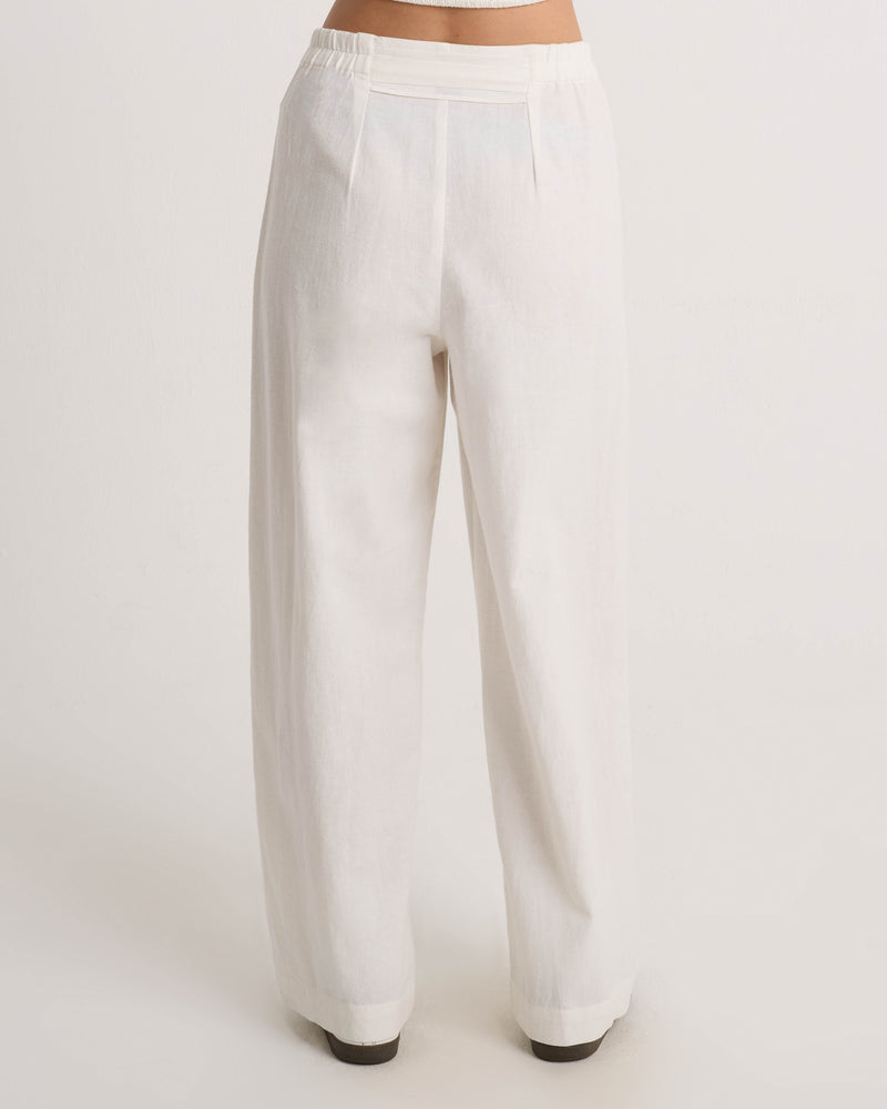 A woman is shown from the back, standing against a white background, modeling Volcom's Women's Bow Chicka Pants—high-waisted, wide leg linen trousers in white.