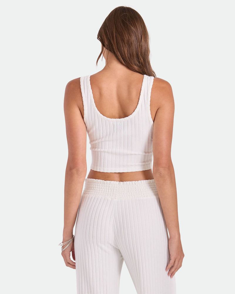 A woman with long brown hair faces away, wearing the Volcom Women's Lounge Bra Tank and matching high-waisted pants—an everyday essential—against a plain white background.