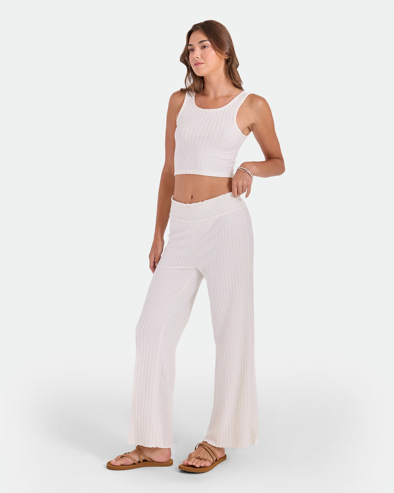A woman with long hair poses against a white background wearing the Volcom Women's Lounge Bra Tank and matching wide-leg pants with sandals, one hand resting on her hip.