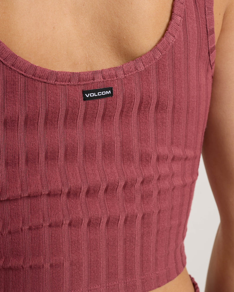 Close-up of a person wearing the Volcom Women’s Sun Lounge Bra Tank, a ribbed, sleeveless crop top in rose. This fitted scoop-neck design highlights the upper back and features a Volcom logo label near the neckline, showcasing its versatility as both a lounge bra tank and layered piece.
