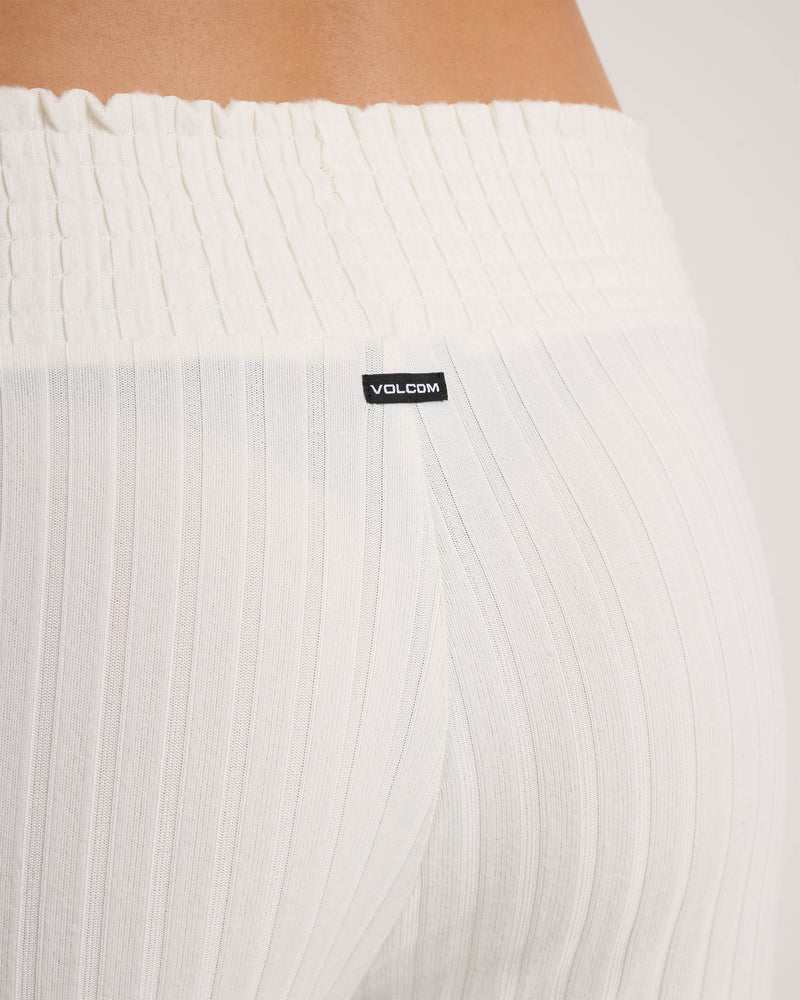 Close-up of a person wearing the Volcom Women’s Sun Lounge Pants in white, featuring a slightly sheer ribbed fabric and a gathered, smocked elastic waistband adorned with a black Volcom label for a relaxed fit.
