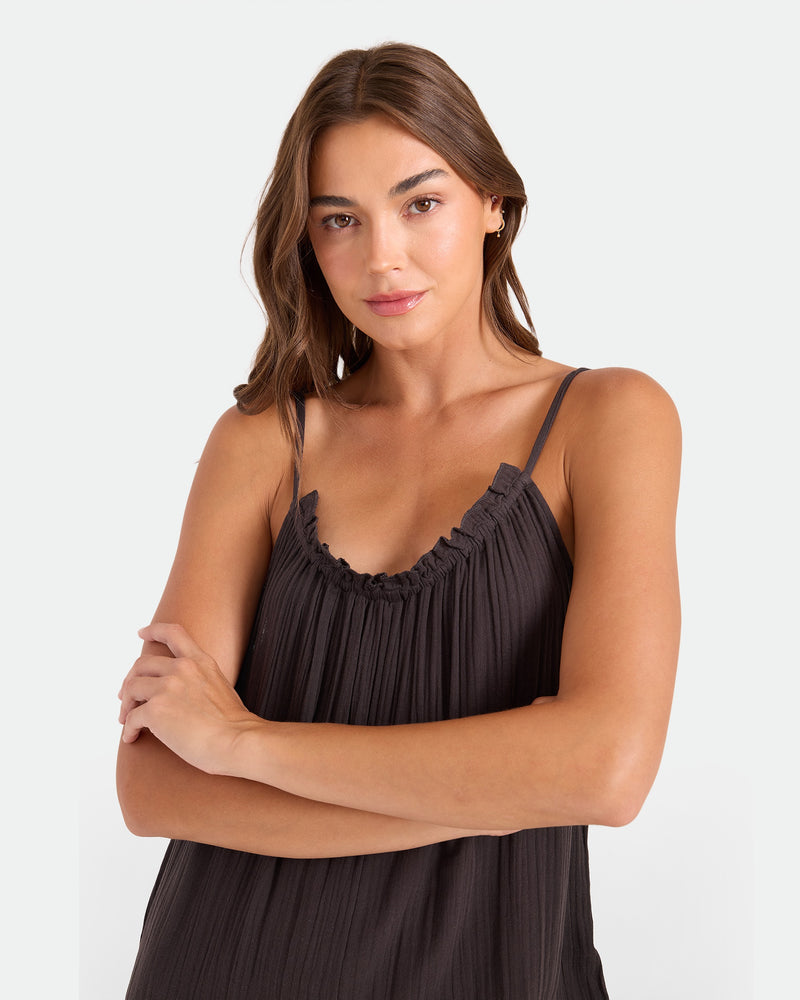 A woman with long brown hair stands confidently with arms crossed, wearing the Volcom Women's Ruffle Up Romper against a plain white background.