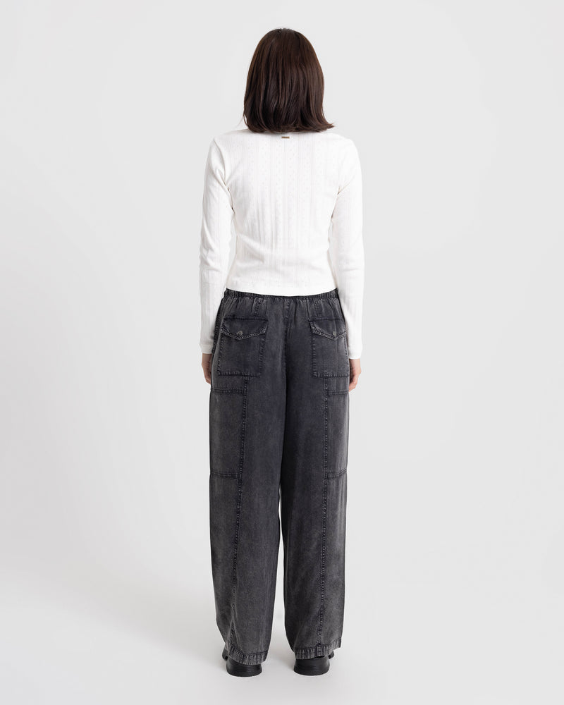 Back view of a person wearing a white long-sleeved shirt and Volcom Women’s Washed Away Twill pants, styled in vintage black with a wide-leg fit and two back flap pockets.