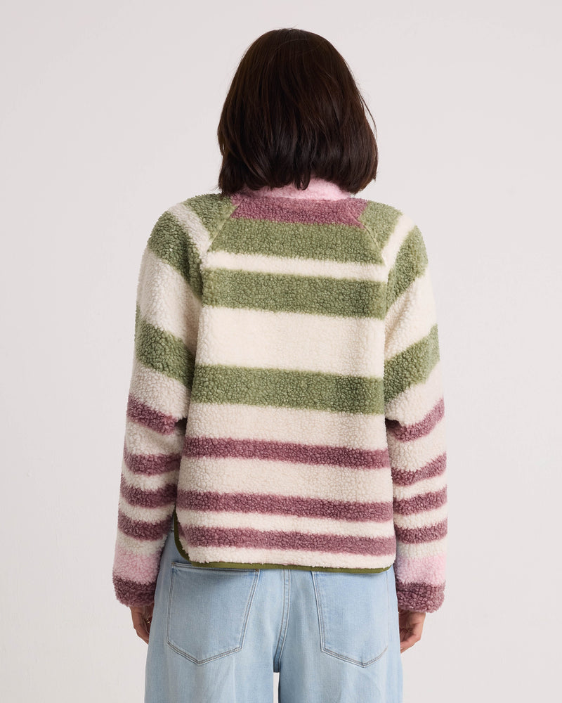 A person with shoulder-length dark hair, seen from behind, is wearing the Volcom Women’s Sherpa Stripe Jacket featuring a boxy fit and horizontal green, white, and purple stripes, paired with light blue jeans against a plain background.