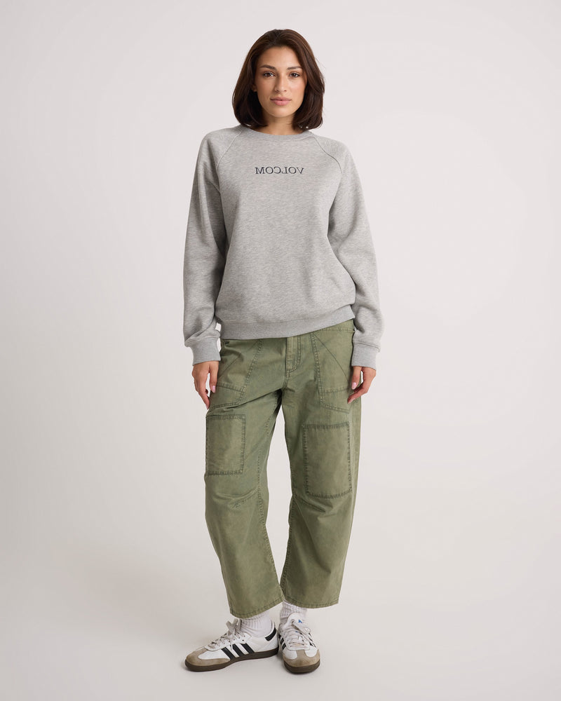 A person wearing a grey cotton silhouette sweatshirt, Volcom Women’s Patchwork Pants, and white sneakers.