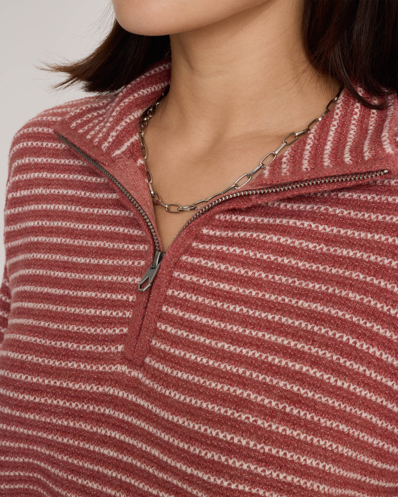 A person wearing the Volcom Women’s Sun Of Sand Sweater, a red and white striped half zip with a boxy fit, paired with a silver chain necklace, shown from the shoulders up.