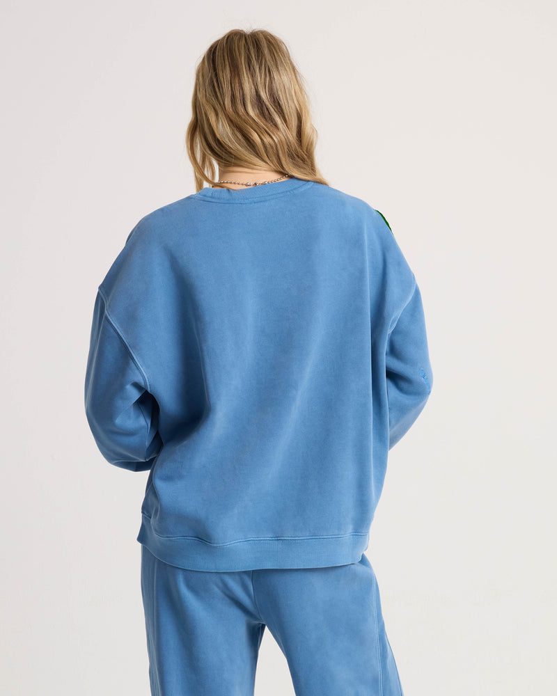 Back view of a person wearing a relaxed, dropped-shoulder blue Women’s Stone Soft Crew sweatshirt and matching sweatpants.