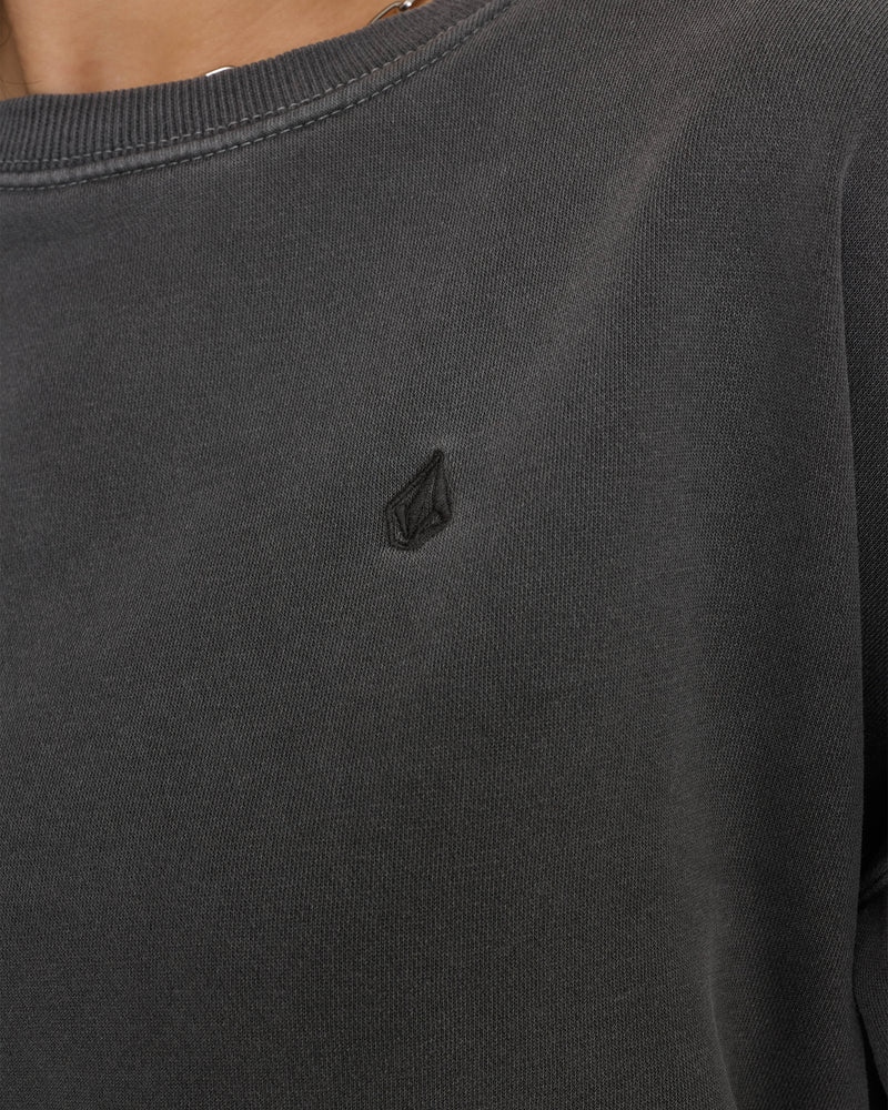 Close-up of the Volcom Women’s Stone Soft Crew sweatshirt in dark grey, featuring a small black embroidered geometric logo on the chest. The image focuses on the collar and shoulder area, showcasing the relaxed fit and premium soft fleece fabric.