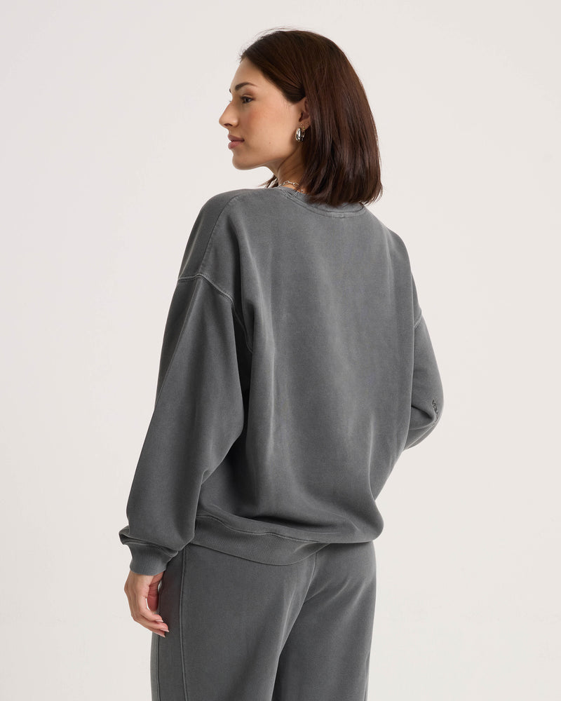 A woman with straight brown hair, dressed in the Volcom Women’s Stone Soft Crew and matching pants in a relaxed fit soft fleece, stands turned slightly to the side against a plain light background.