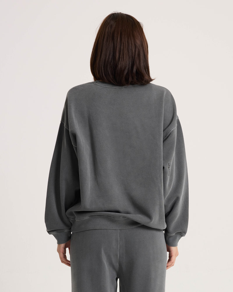 A model with shoulder-length brown hair is shown from the back against a plain light background, wearing the Volcom Women’s Stone Soft Crew in dark gray along with matching soft fleece pants in a relaxed fit.
